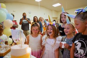 Children celebrating at a birthday party with balloons and cake in a community room.
