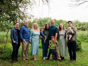A group of people wearing casual attire pose together outdoors in a grassy field with trees in the background.