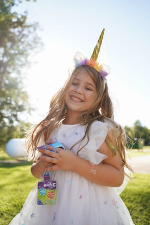 Young party guest in a unicorn headband and white dress enjoying a sunny celebration outdoors.