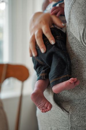 Close-up of tiny baby feet and jeans against a grey sweater.