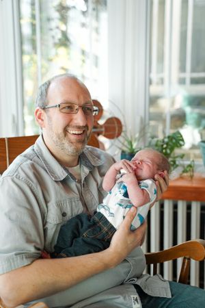 A caring moment between parent and newborn in a sunny room with houseplants.
