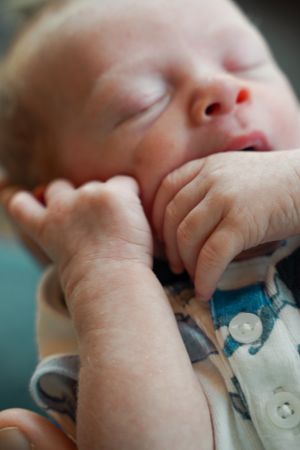 Peaceful sleeping newborn baby in close-up showing tiny hands and features.