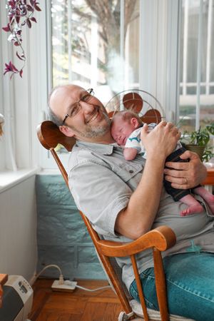 Tender moment in a rocking chair by window with houseplants visible.