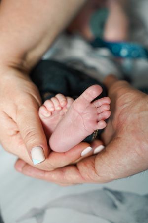Gentle hands cradling tiny newborn baby feet in soft lighting.