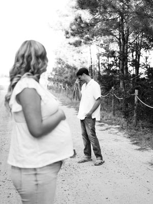A black and white series of four photos showing a couple walking together on a dirt path through trees.