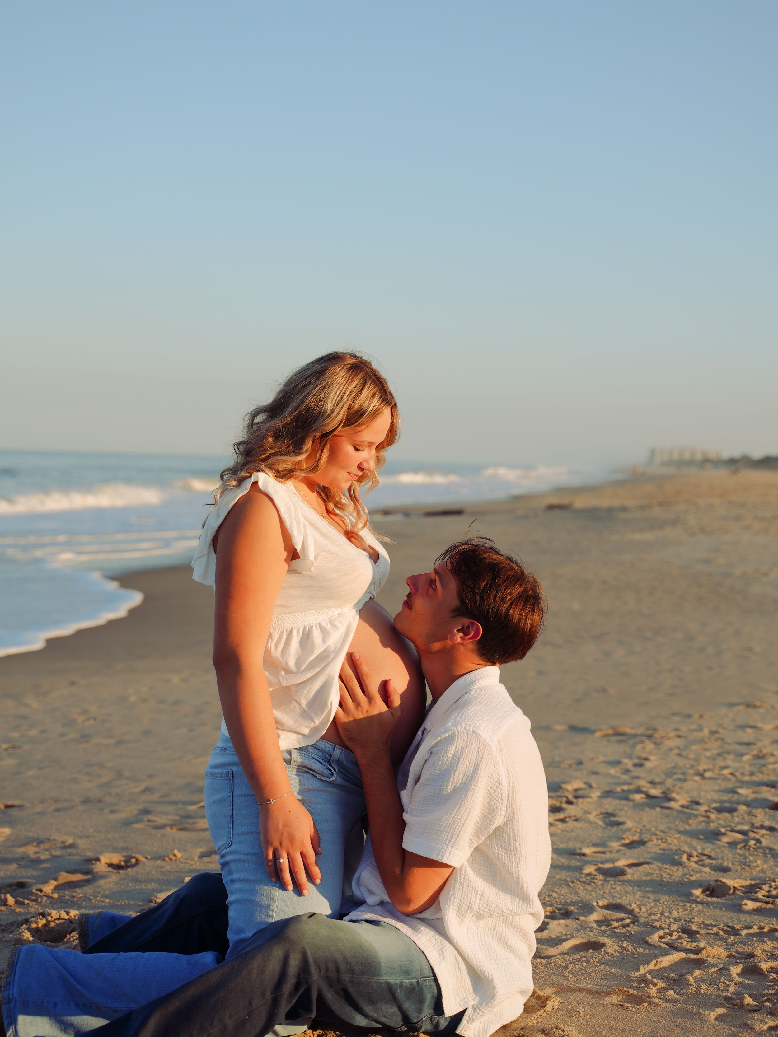 A couple shares an intimate moment together on a sandy beach during sunset.