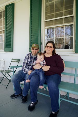 A family sits together on a teal-colored porch bench with green shutters visible in the background.