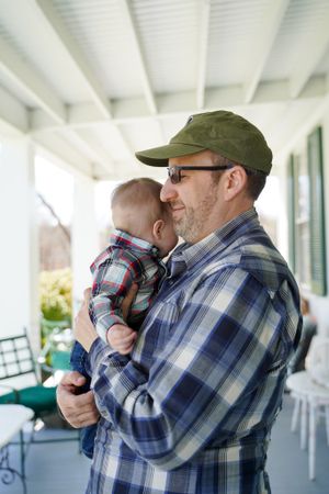 Casual outdoor portrait on a white porch with green shutters featuring tender family moment.