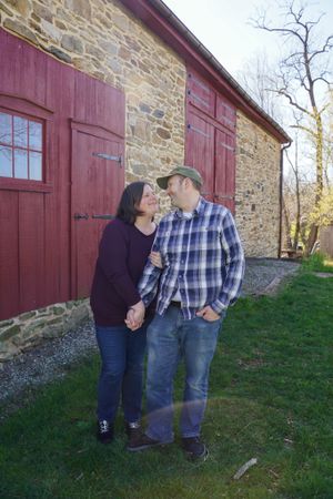 Romantic moment shared between couple against stone barn with red doors.