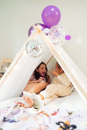 Children playing in white tent fort decorated with purple balloons and disco ball.