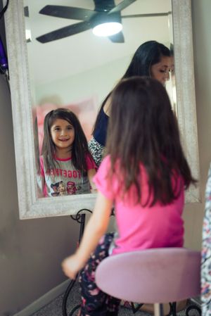 Mirror reflection shows bright smile while sitting at vanity with ceiling fan visible.