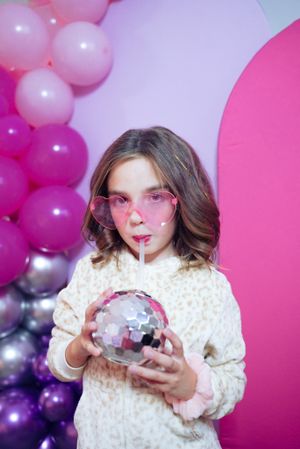 Party setup with pink balloon arch and disco ball against vibrant pink and purple background.