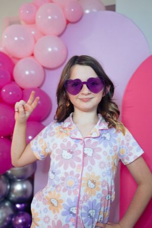 Playful pose with peace sign against pink balloon arch and purple backdrop.