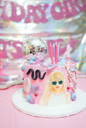 Pink birthday cake decorated with disco ball, candles and cartoon character design.