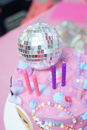 Close-up of disco ball and colorful candles on pink frosted birthday cake.
