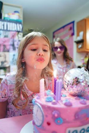 Blowing out candles on pink birthday cake with disco ball decoration.