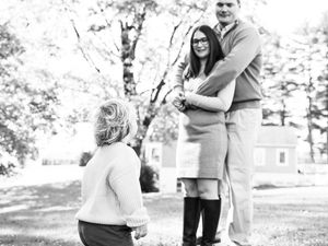 A couple embraces and smiles during an outdoor engagement photo session in a sunlit park setting.