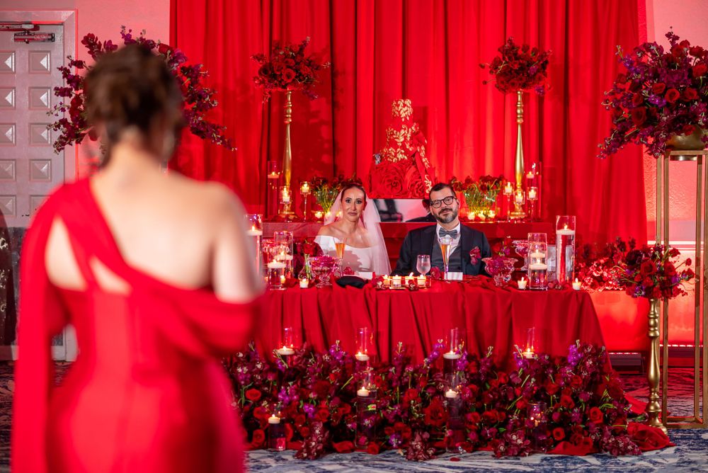 Wedding reception setup with red backdrop, floral arrangements and bar area.