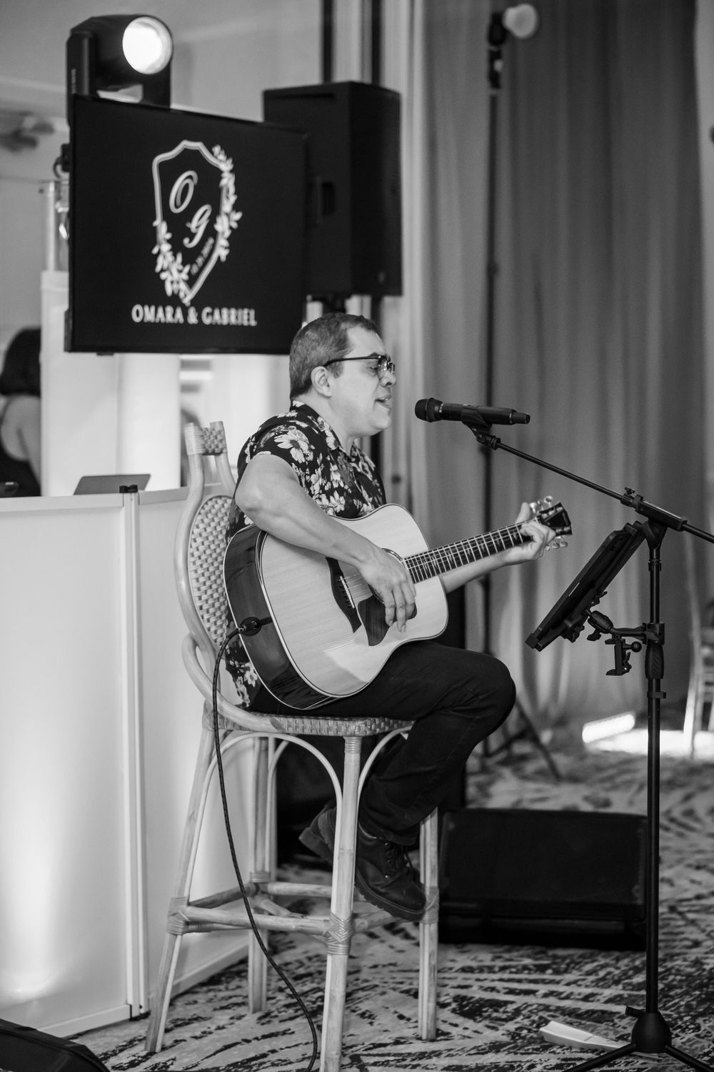 Black and white photo of acoustic guitarist performing at event with professional lighting setup.