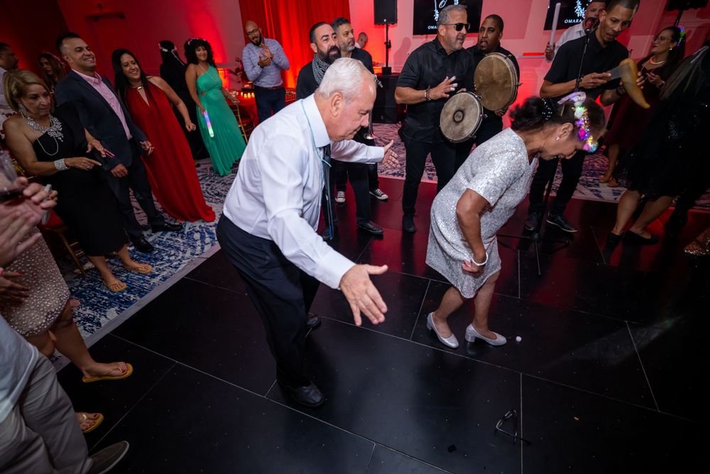 Guests dance energetically on dark dance floor with red ambient lighting at reception.