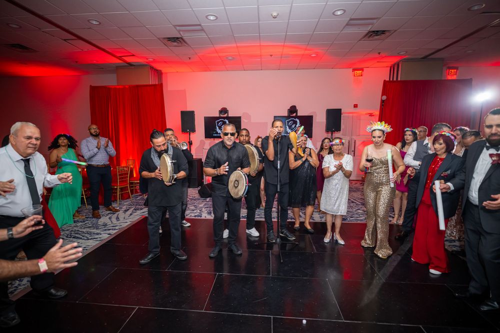 Wedding band plays instruments while guests dance in red-lit reception space.