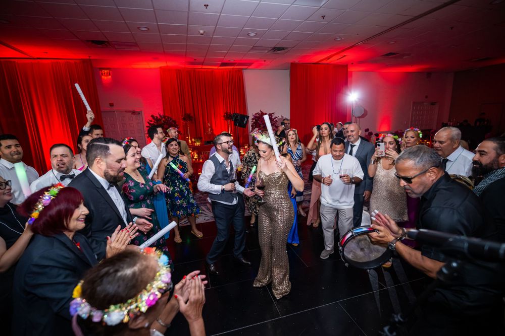 Wedding guests fill dance floor while celebrating with light-up props under red lighting.