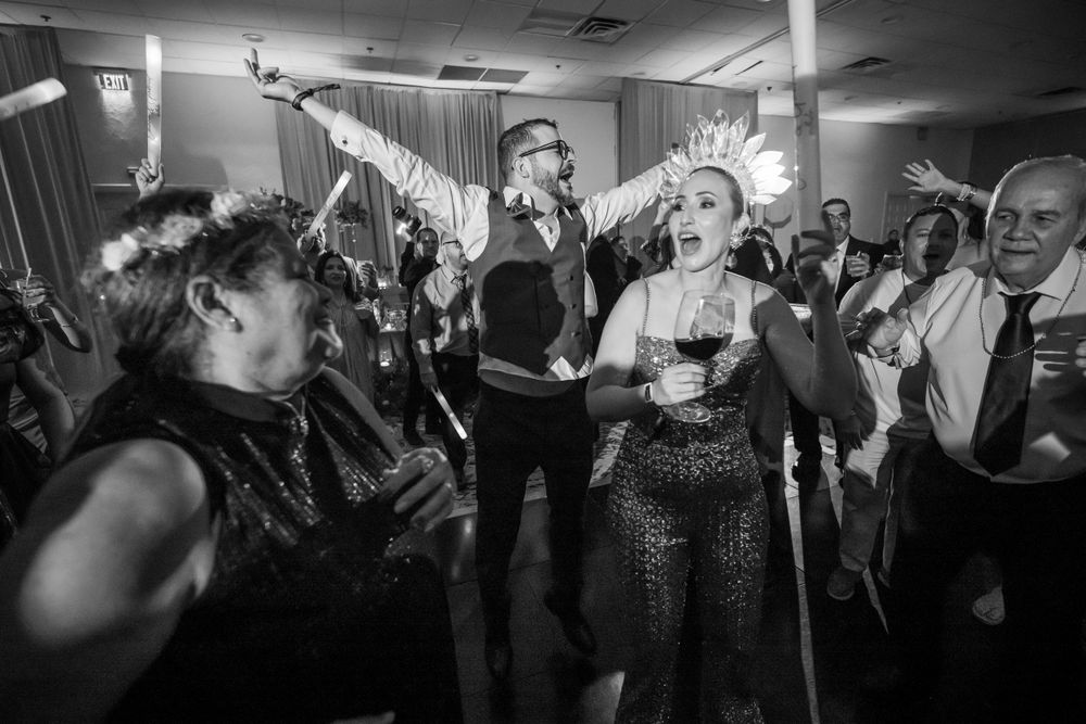 Wedding guests dance energetically on a dimly lit dance floor at a reception celebration.