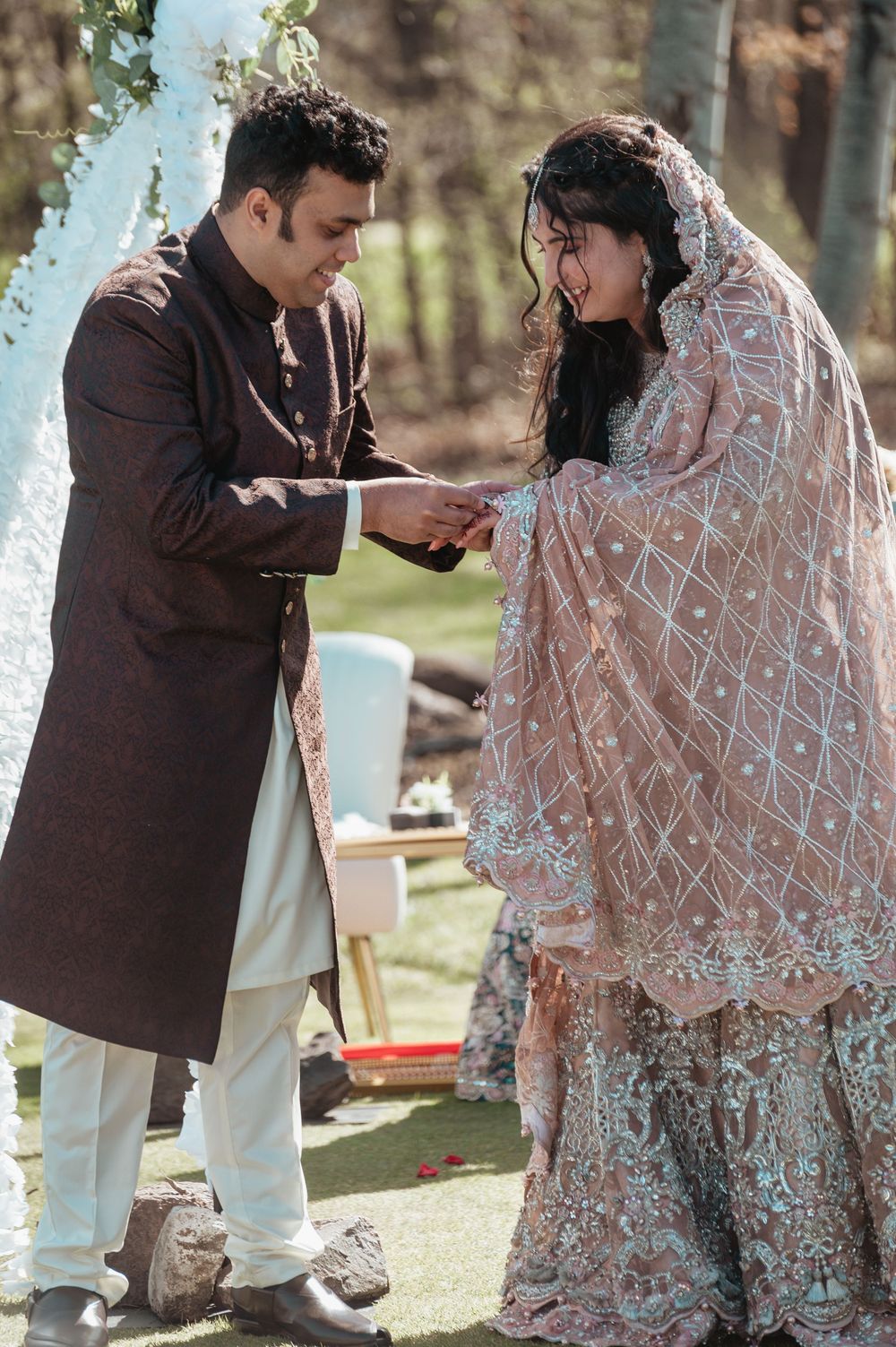 Couple exchanging rings at outdoor South Asian wedding, bride in pink embroidered lehenga.
