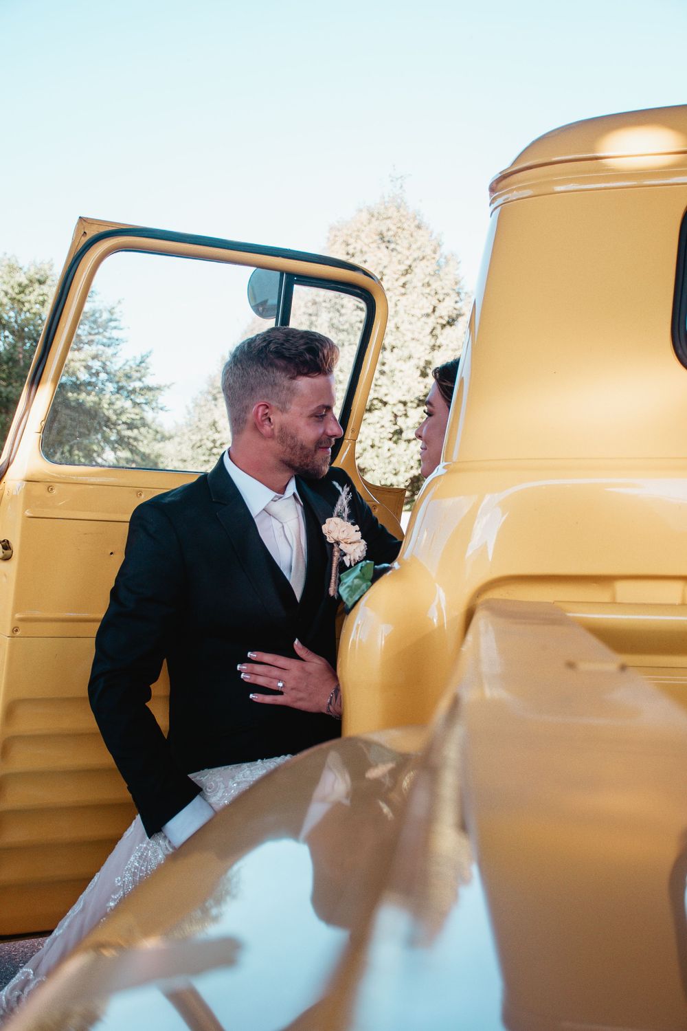 A stylish couple poses next to a vintage yellow pickup truck on their wedding day.