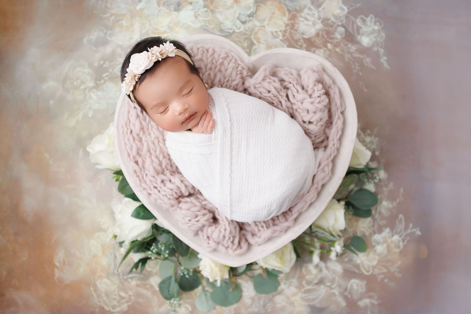 Newborn photography setup with soft pink wrap and floral arrangements in vintage style.