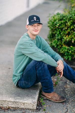 Person in mint green sweatshirt and baseball cap sitting on concrete curb.