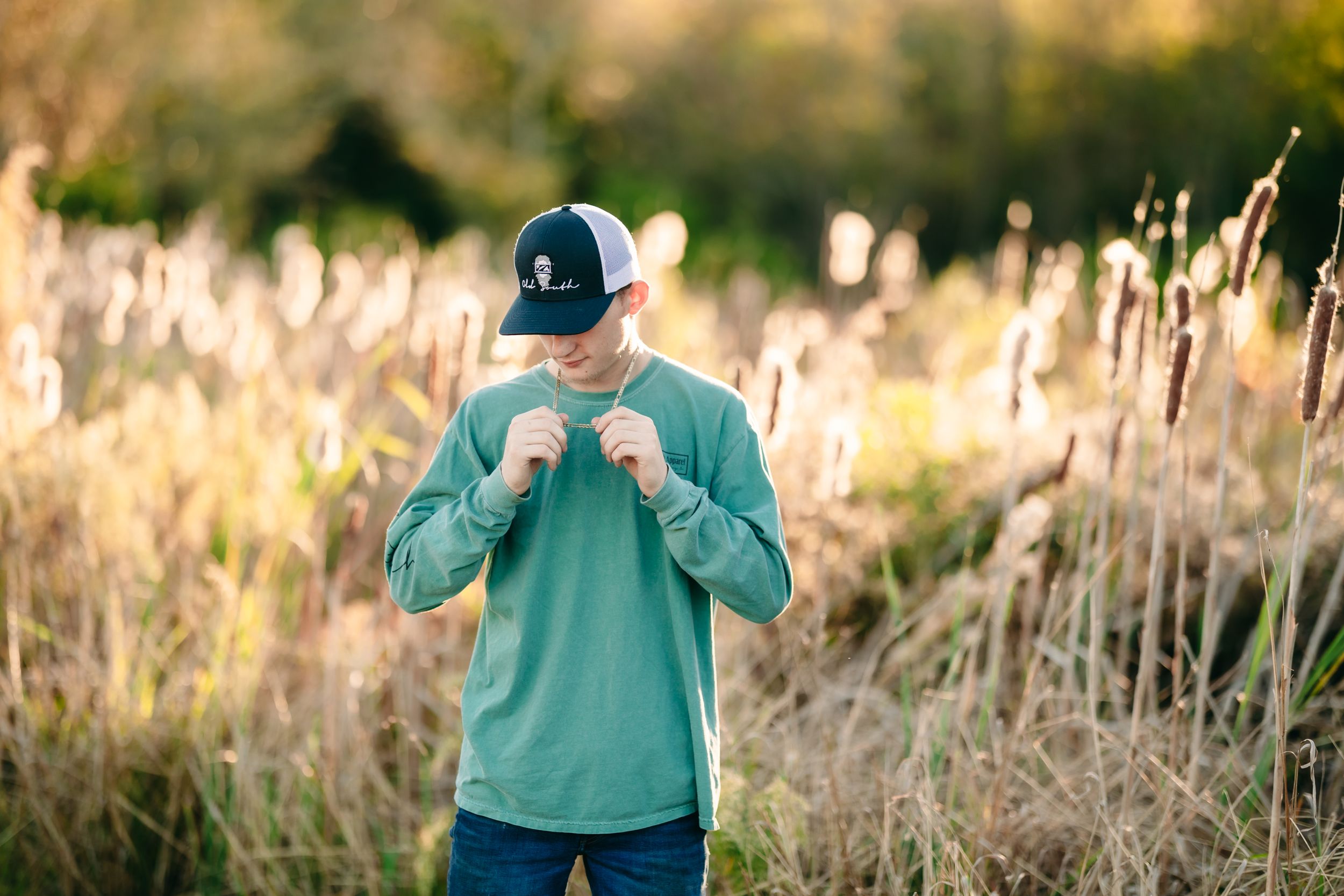Back view of person in mint green sweatshirt and cap standing among tall grass.