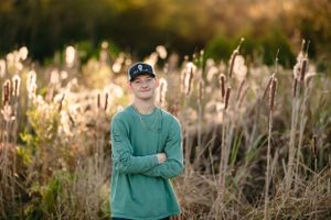 Person in green sweatshirt stands among tall cattails at golden hour.