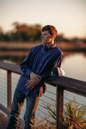 Person in navy button-down shirt leaning on wooden dock railing at sunset.