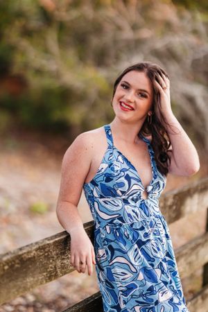 Portrait in a blue and white patterned summer dress against a natural outdoor backdrop.