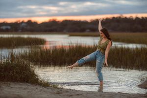 Person in casual denim and green top splashing in marsh water at sunset.