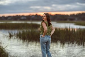 Person wearing denim and olive top poses by marsh waters at golden hour.