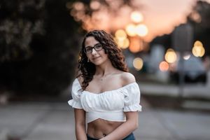 Portrait of woman in white off-shoulder top against blurred sunset bokeh background.