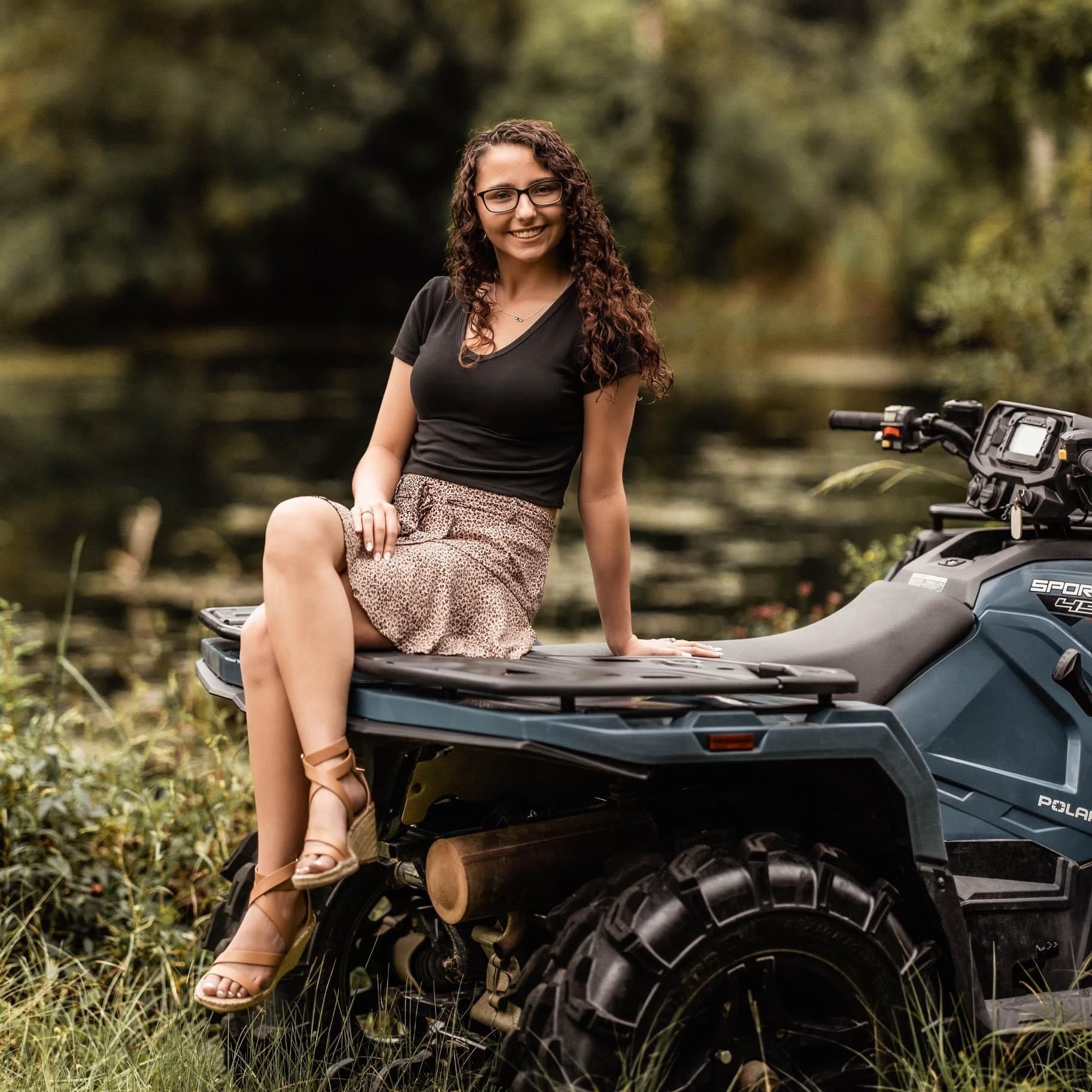 Casual portrait of woman sitting on ATV in natural outdoor setting.