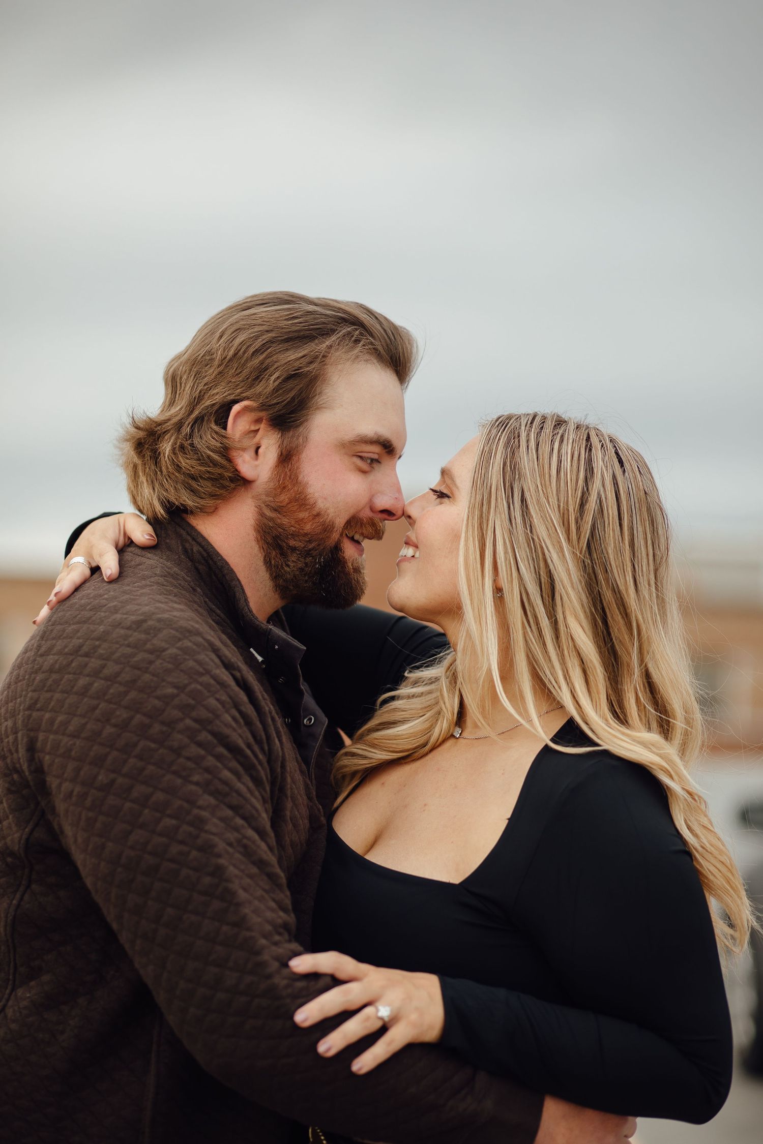 A romantic couple embraces outdoors, sharing an intimate moment against a cloudy sky.