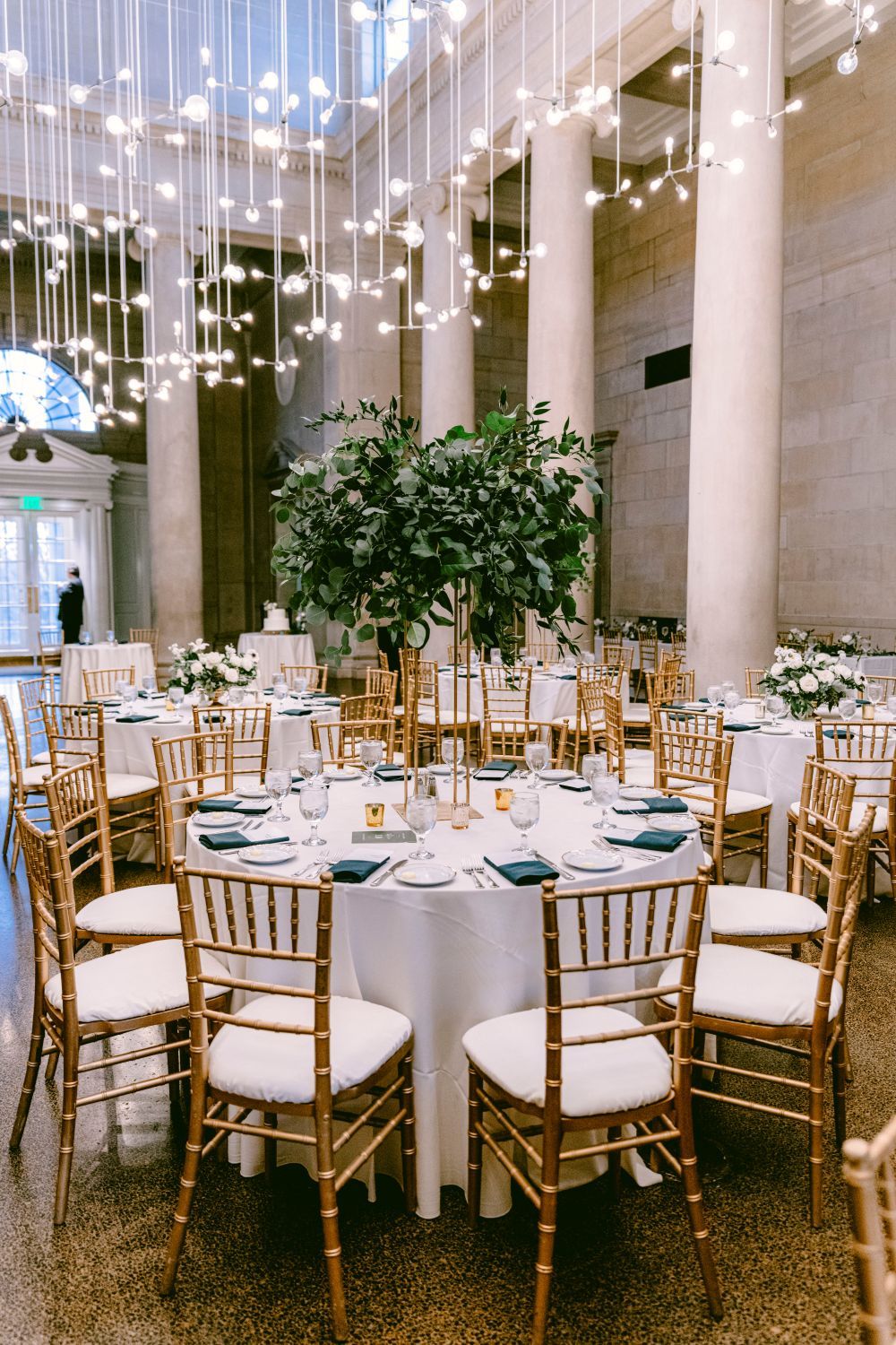 Elegant wedding reception venue with white string lights, gold chiavari chairs, and round tables set for a formal dinner.