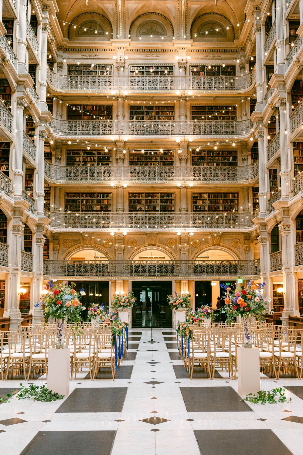 Elegant wedding ceremony setup inside historic Baltimore Peabody Library with ornate multi-level balconies and gold details.
