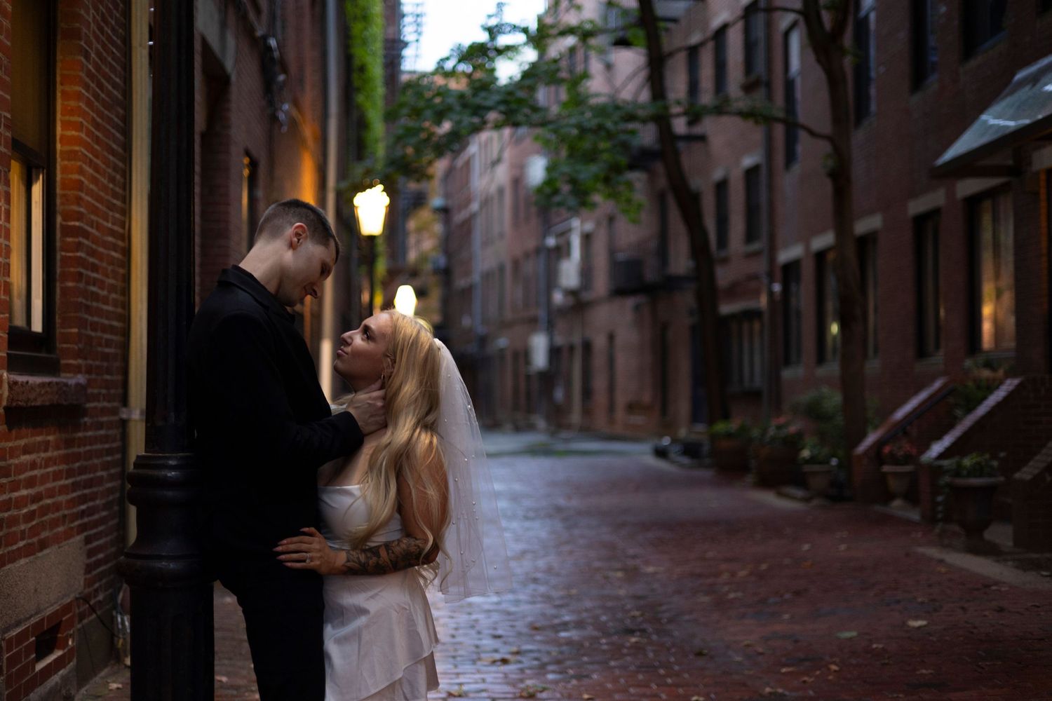 Historic brick buildings line a narrow cobblestone street in Boston's Beacon Hill neighborhood at dusk.