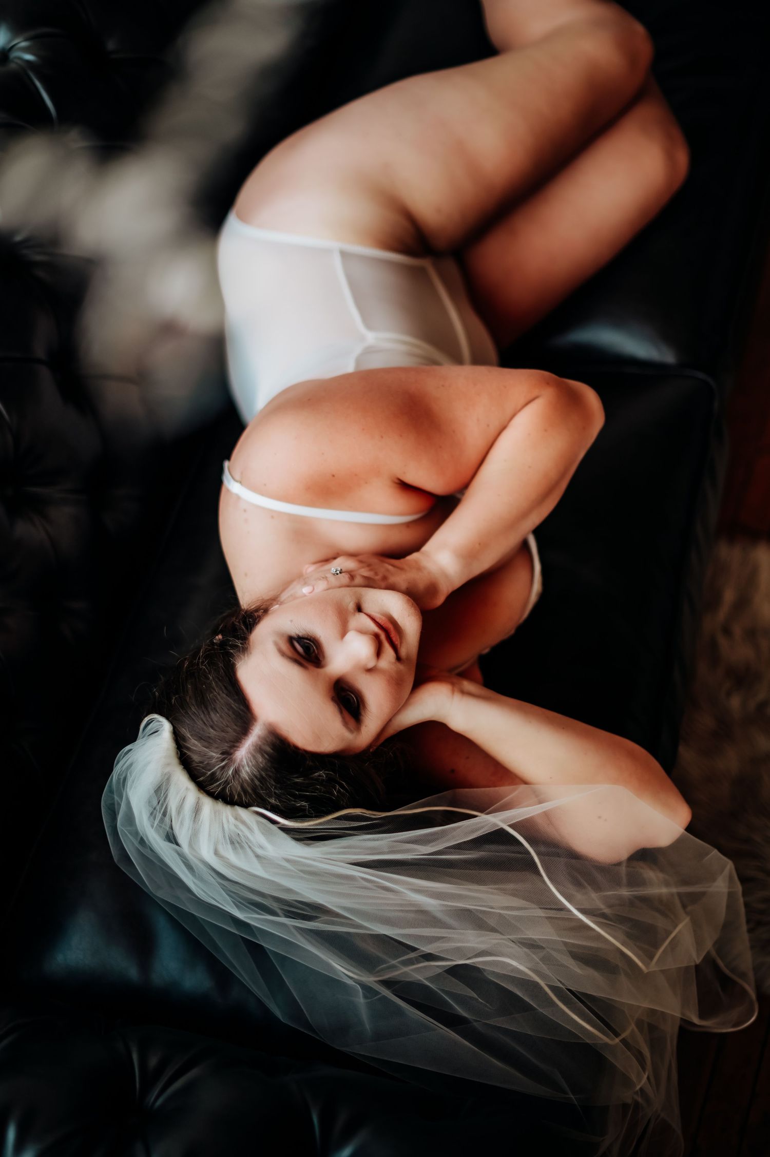 Artistic boudoir photography featuring ethereal white veil and lingerie in moody lighting from above.