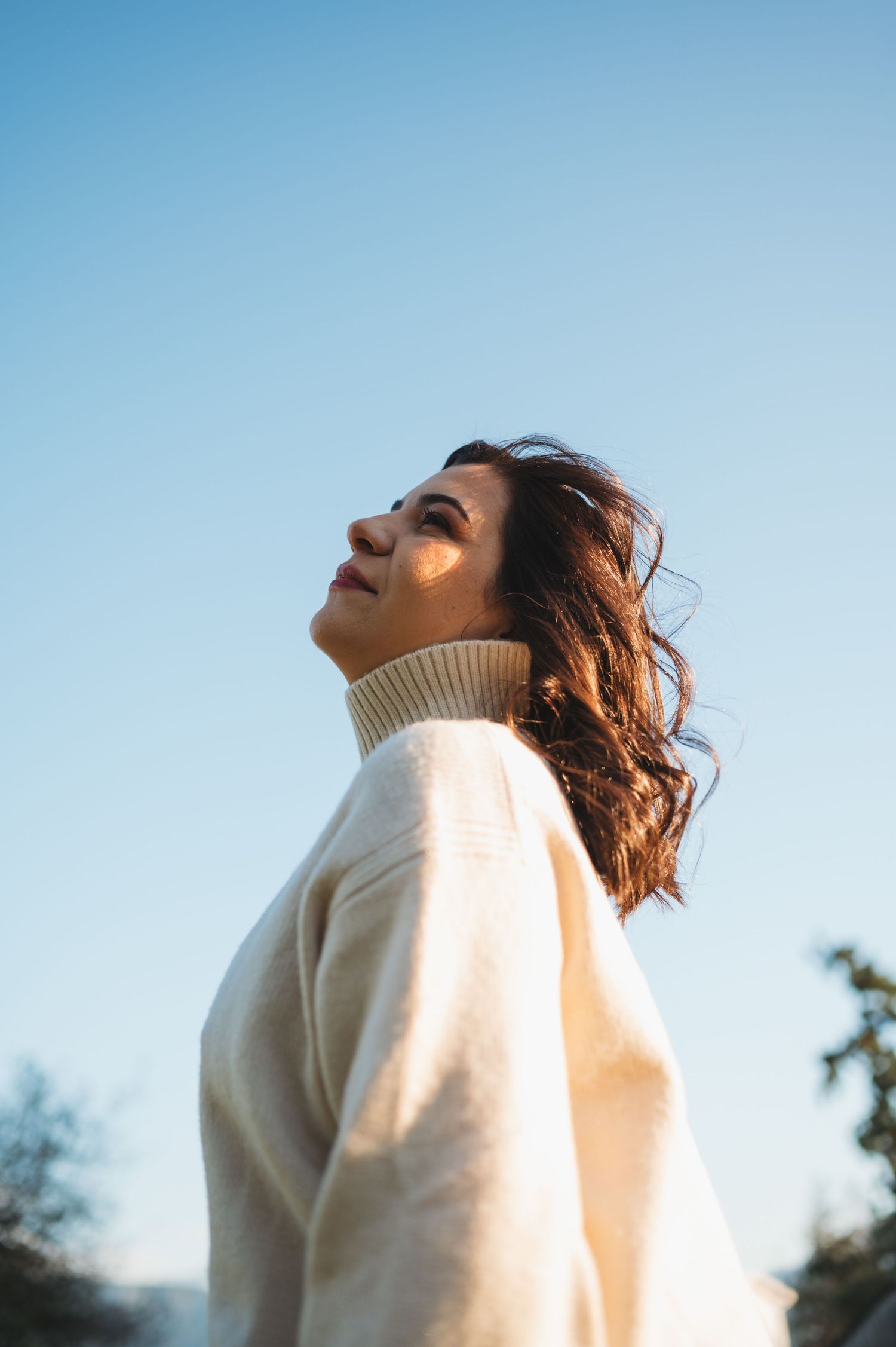 Person in white sweater basking in sunlight against blue sky backdrop.
