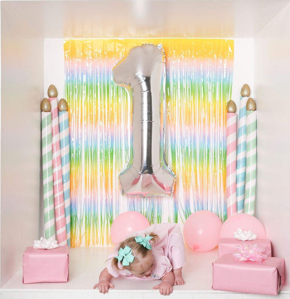 Rainbow streamer backdrop with pink party decor and straws creates a festive unicorn-themed celebration setup.