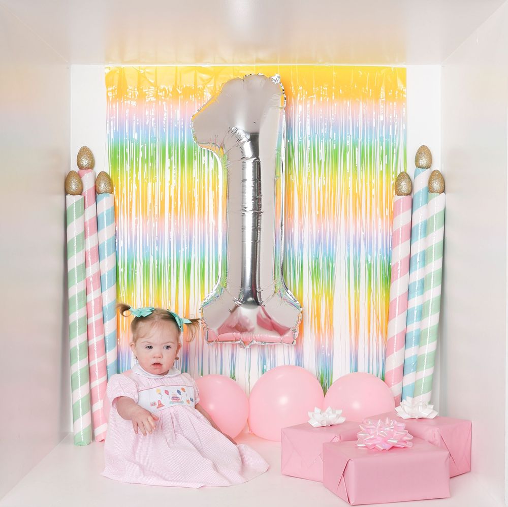 A pink and rainbow themed party backdrop with striped straws and glittery decorations creates a festive atmosphere.