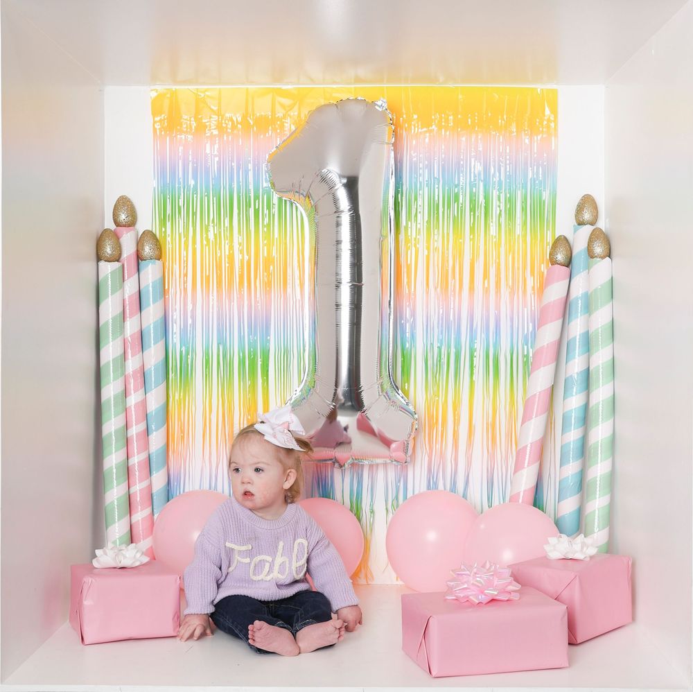 Colorful rainbow curtain backdrop with pink decorative boxes and striped paper straws for party staging.