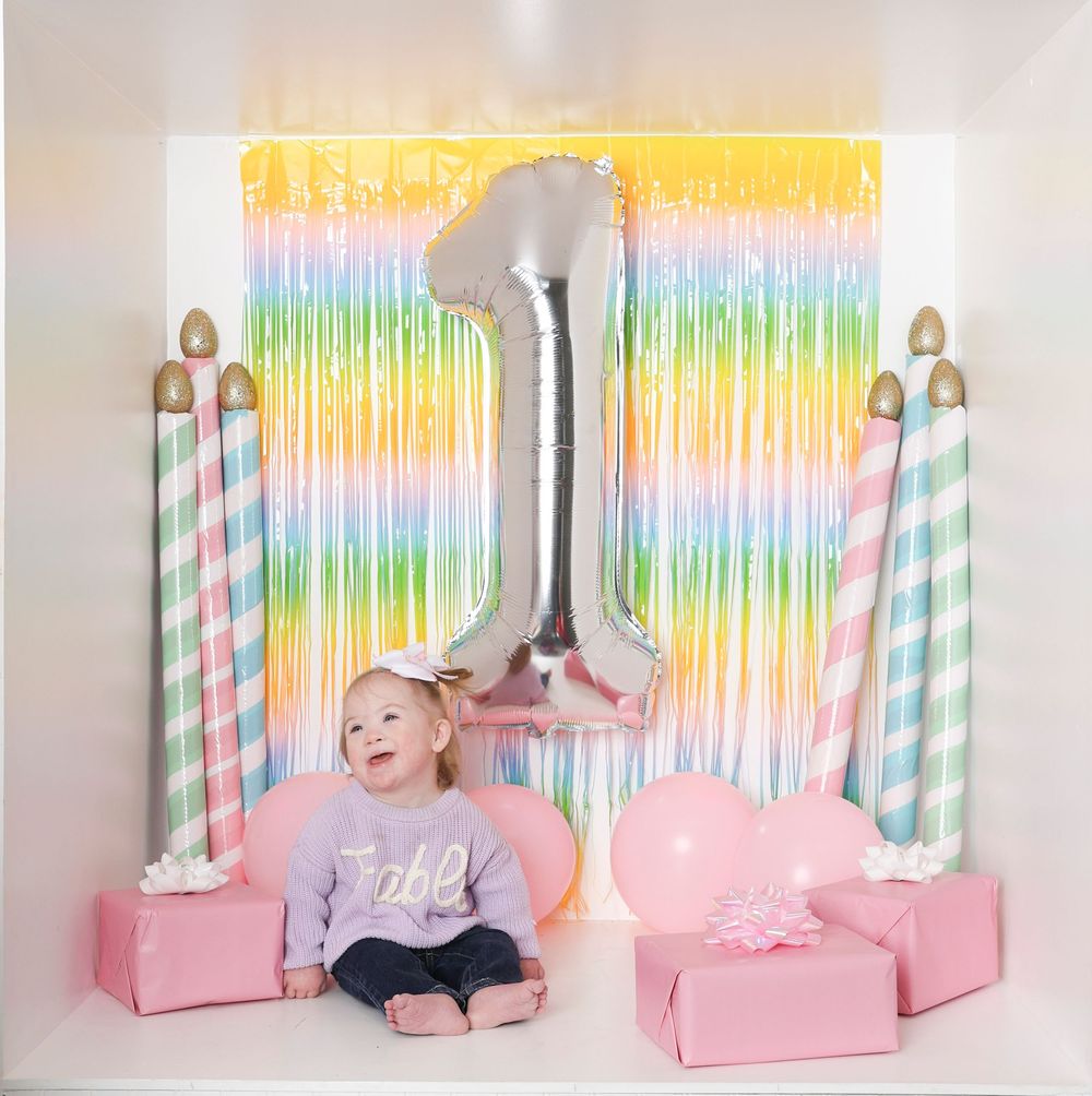 Colorful rainbow backdrop with pink decorative elements and striped candle props for a festive party setup.