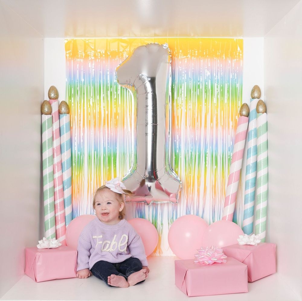 Colorful birthday party setup with iridescent backdrop, striped candle decorations, and pink gift boxes.